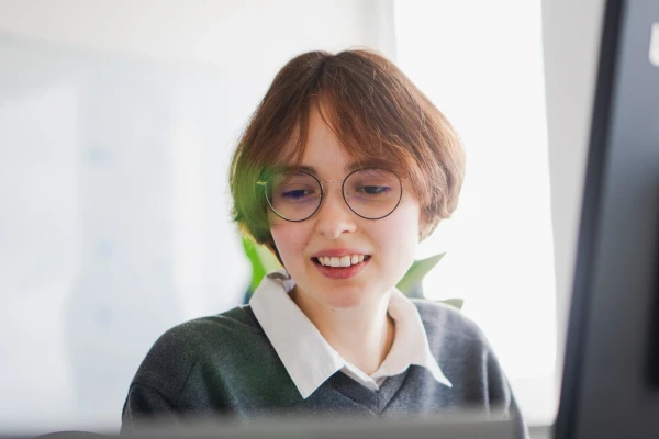 Eine junge Frau mit Brille und brauenen Haaren sitzt an einem Arbeitsplatz | SPIRIT/21