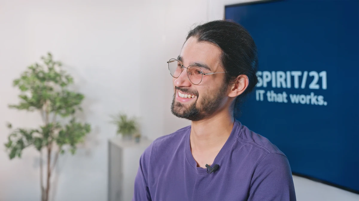 Ein junger Mann mit dunklen Haaren und Brille im Interview. Im Hintergrund ist das SPIRIT/21-Logo sowie eine Pflanze ersichtlich. | SPIRIT/21