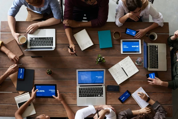 Vogelperspektive auf einen Konferenztisch, an welchem acht Personen sitzen und mit Stift und Papier oder Laptops arbeiten | SPIRIT/21