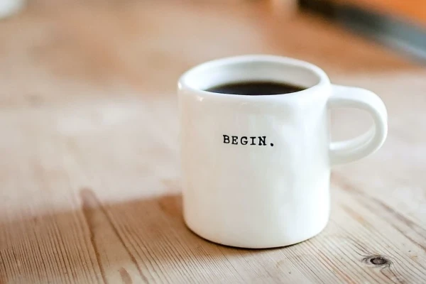 Eine weiße Tasse auf einem Holztisch mit dem Schriftzug "Begin". | SPIRIT/21