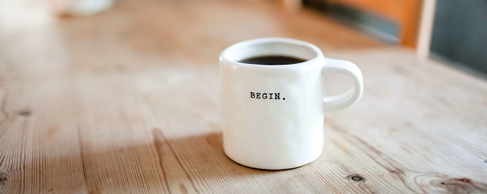 Eine weiße Tasse auf einem Holztisch mit dem Schriftzug "Begin". | SPIRIT/21