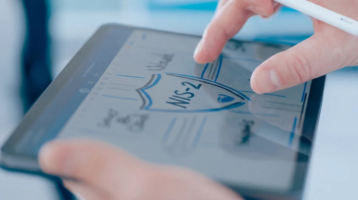 Nahaufnahme eines Tablets, auf dem mit einem Eingabestift eine Skizze mit einem Schildsymbol und der Aufschrift NIS‑2 gezeichnet wird. | SPIRIT/21